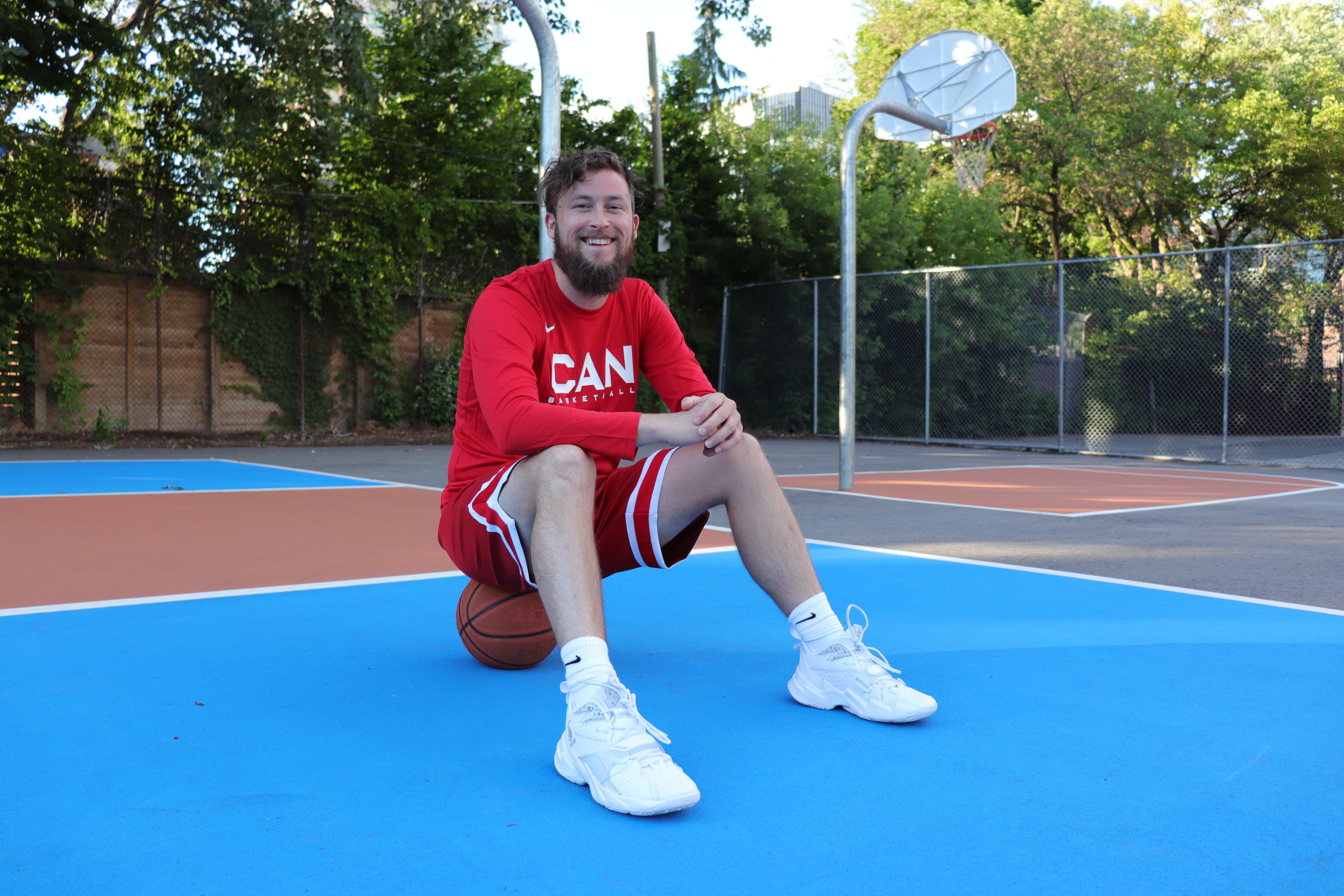 Nolan Knill sitting on a basketball on an outdoor court